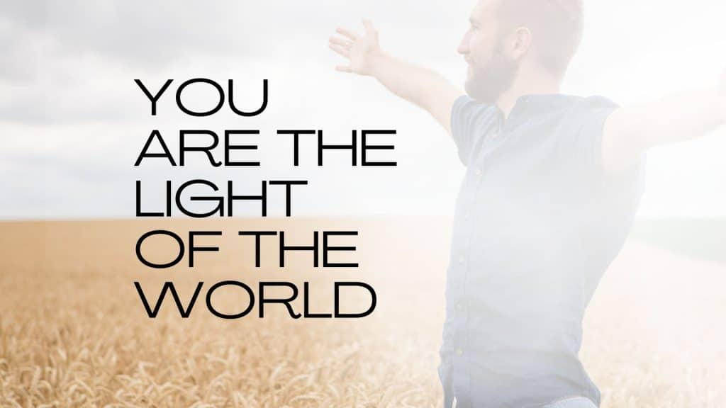 man in bright light, standing with arms stretched out over a wheat field